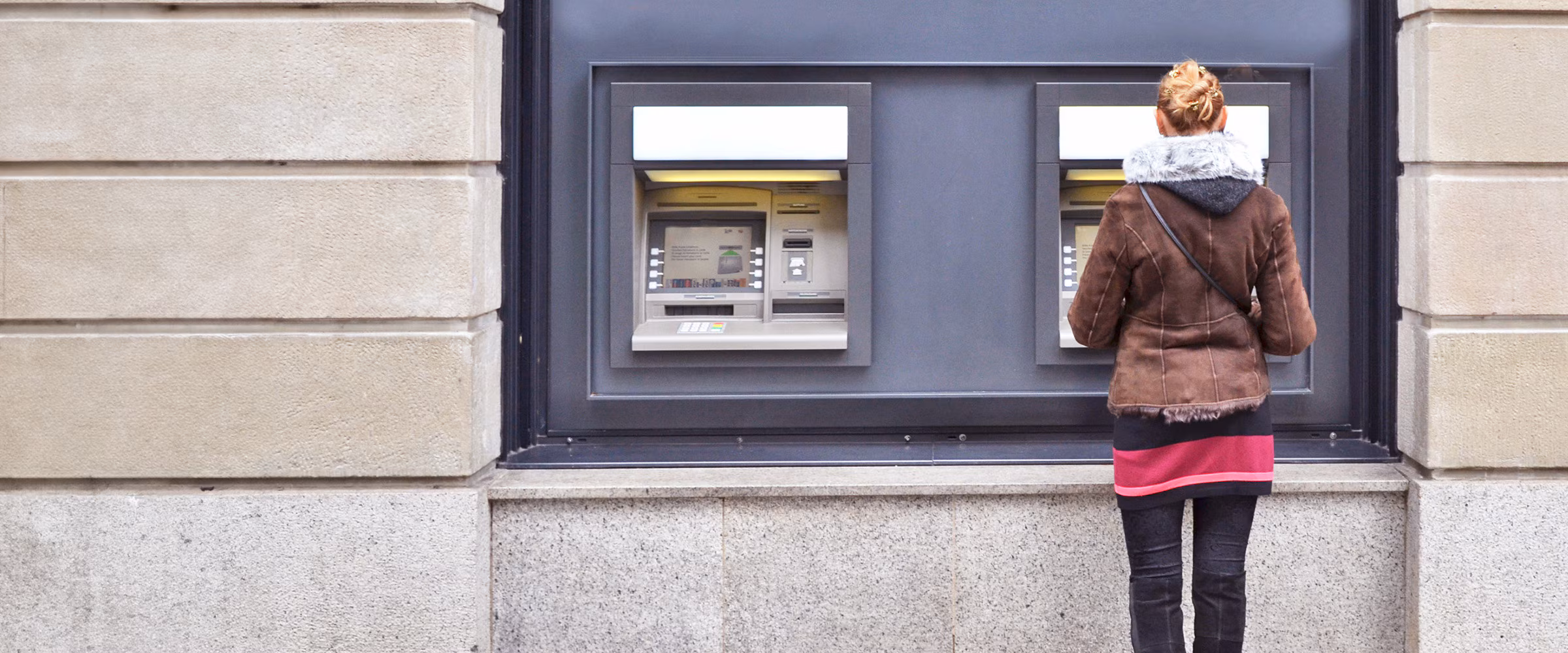 Photo of a woman standing in front of a bank's ATM machine.
